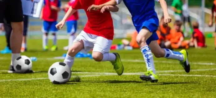 Youth soccer coach kneeling to tie a player&#39;s cleat on the sideline before a practice for youth sports insurance and coach insurance